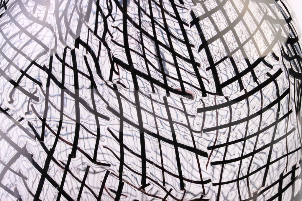 Detail view of a glass vessel with black lines and bubbles.